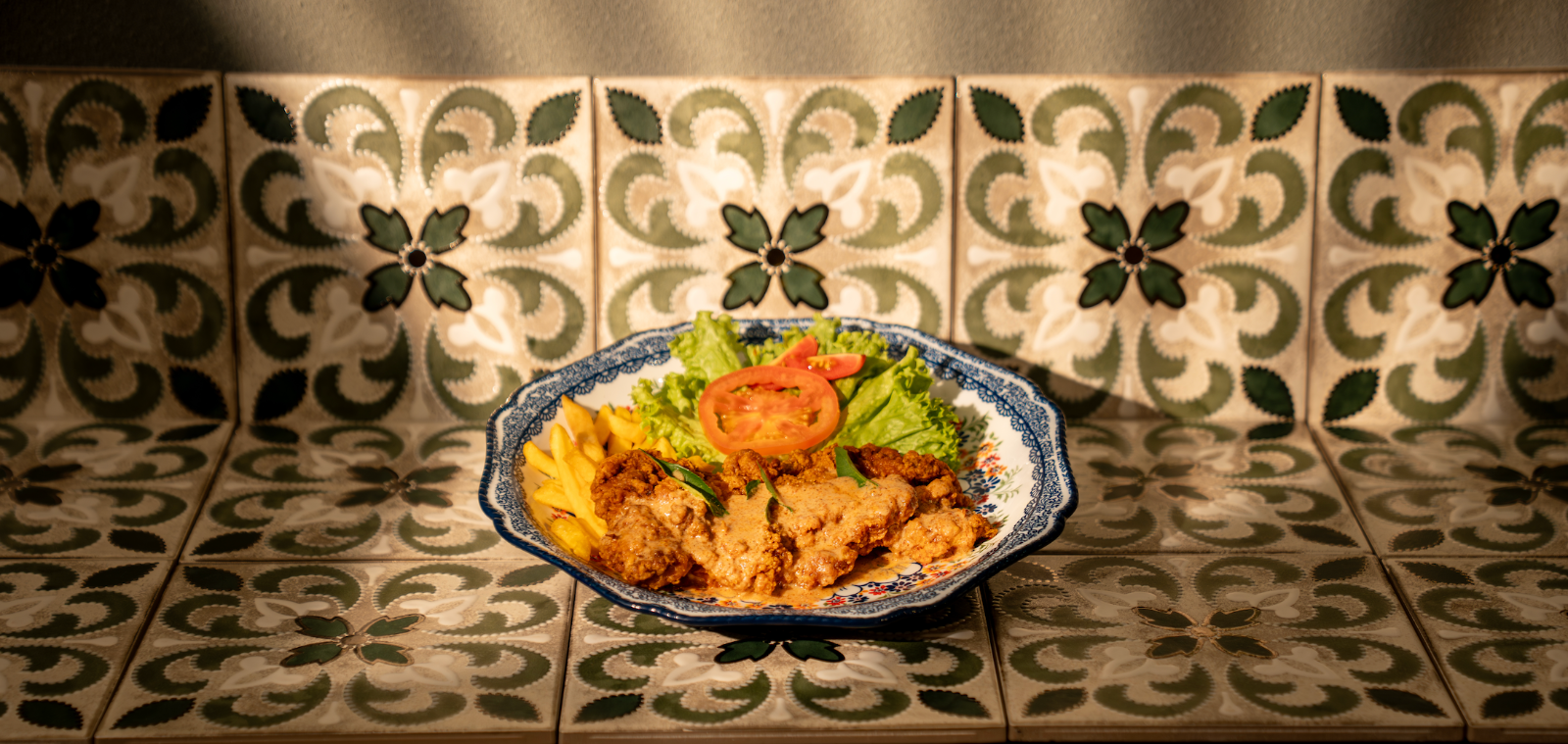 Hainanese chicken chop with curry sauce and fries on a heritage tile counter