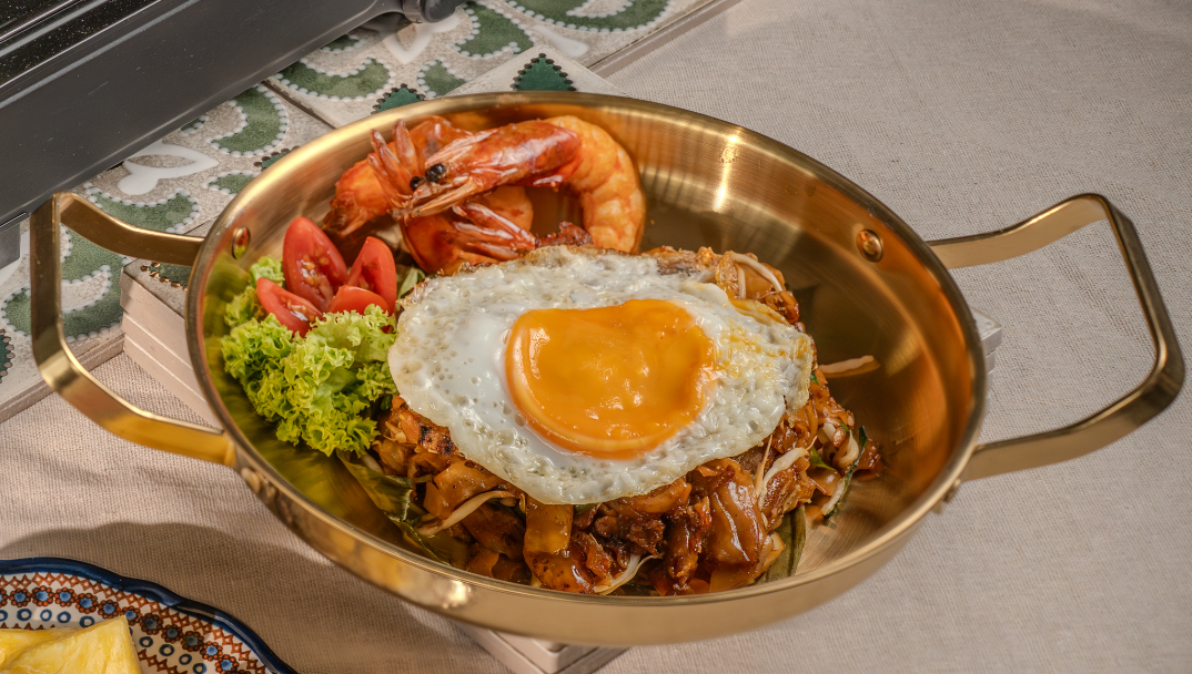 Char kuey teow with prawns and a fried egg served in a brass pan